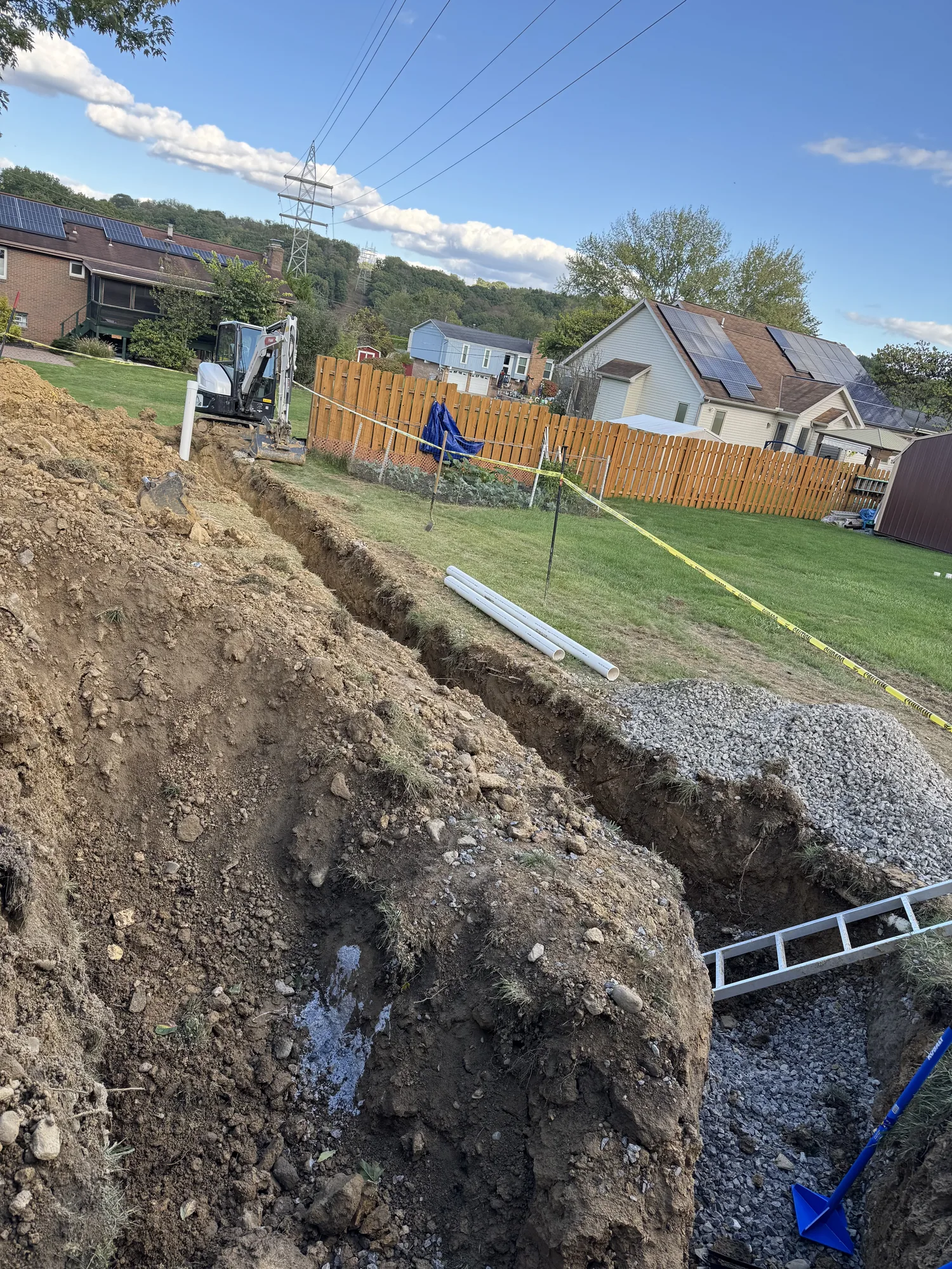 Open utility trench with stone bedding and staged PVC pipe in an Allison Park back yard
