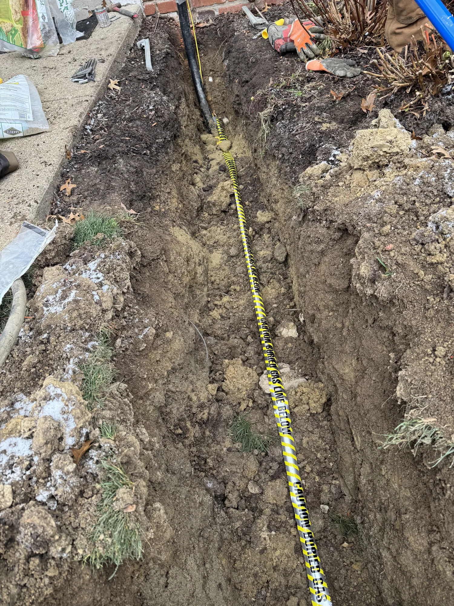 Open trench with buried gas line marker tape over new poly gas pipe at a Pittsburgh area home