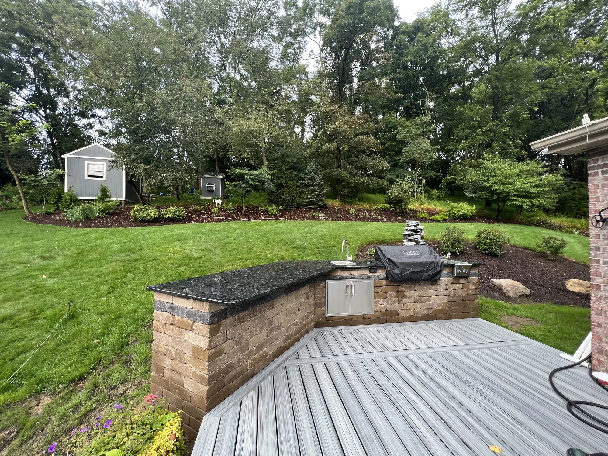 Stone outdoor kitchen with granite counter and built in grill off a composite deck in Allison Park