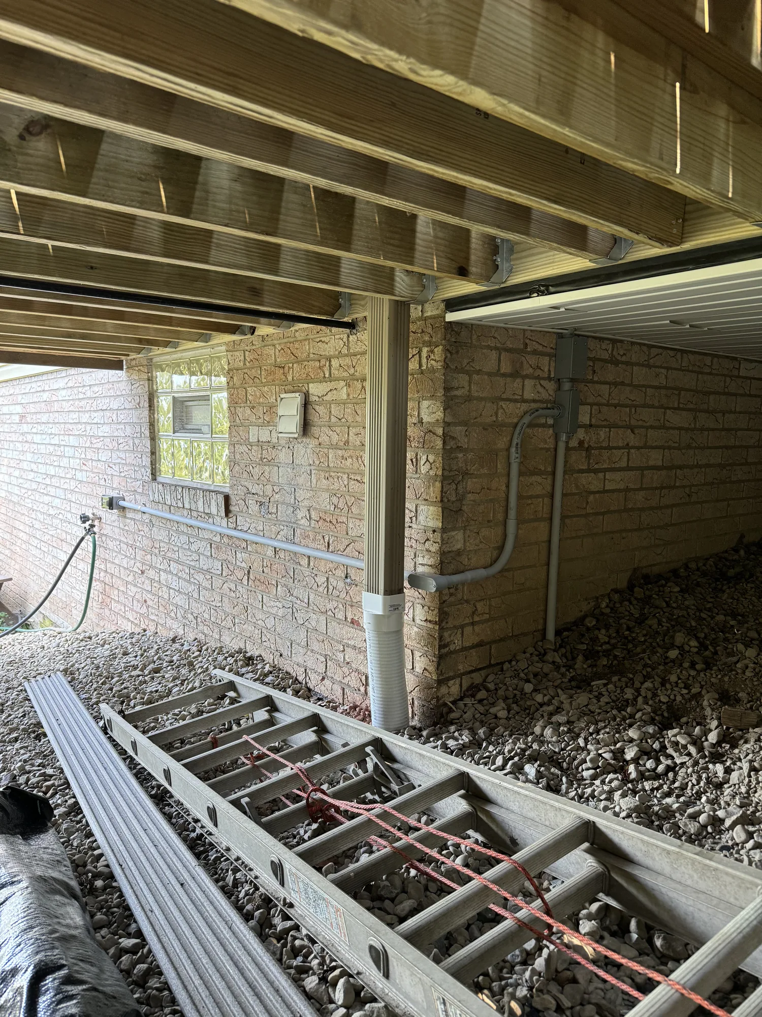 Downspout drain line piped down a foundation wall into a gravel drainage bed at a Pittsburgh home