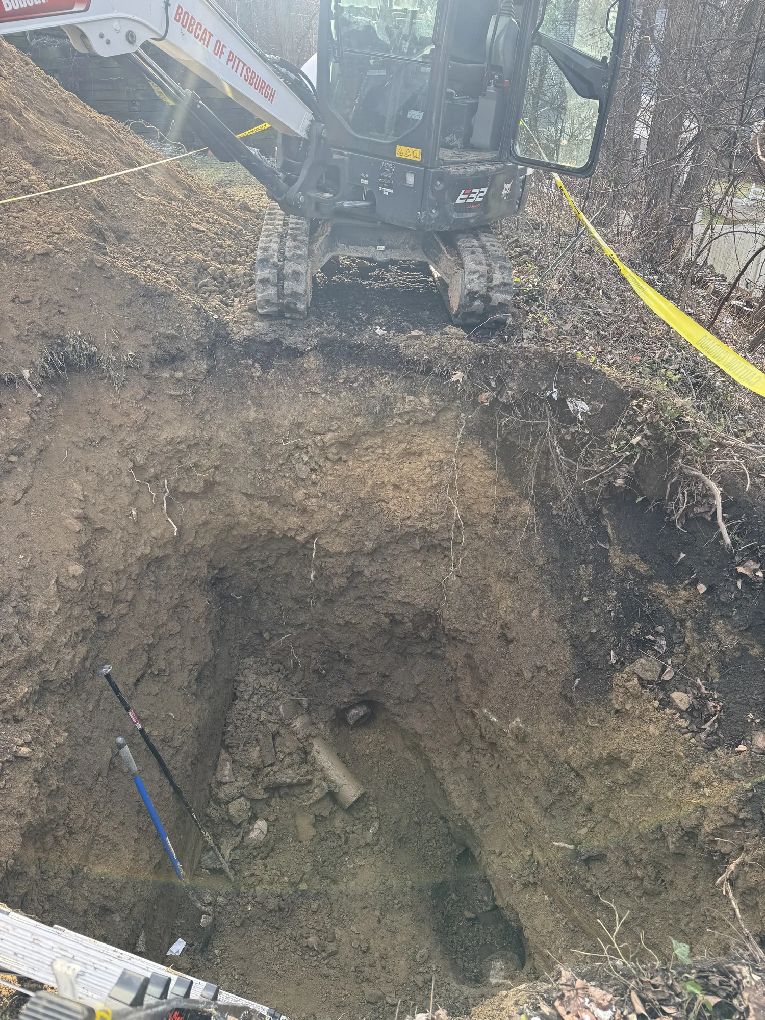 Mini excavator uncovering an old clay sewer line in a trench at a Pittsburgh area property
