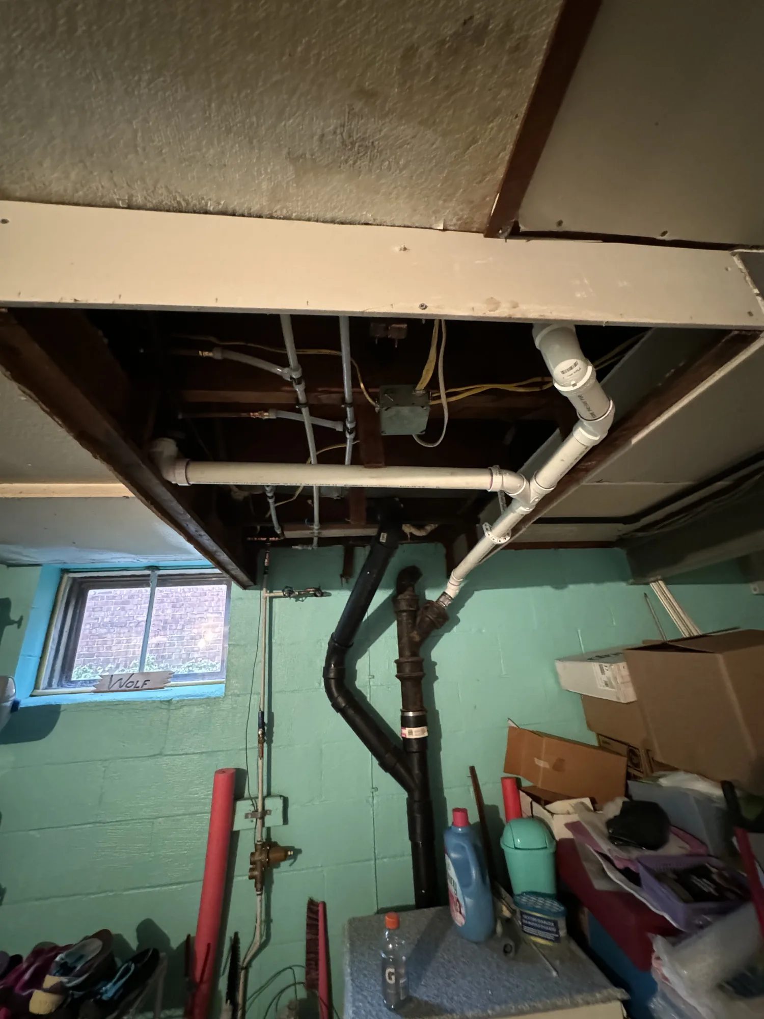 Basement wall opened to expose PVC drain lines and a cast iron stack during a repipe