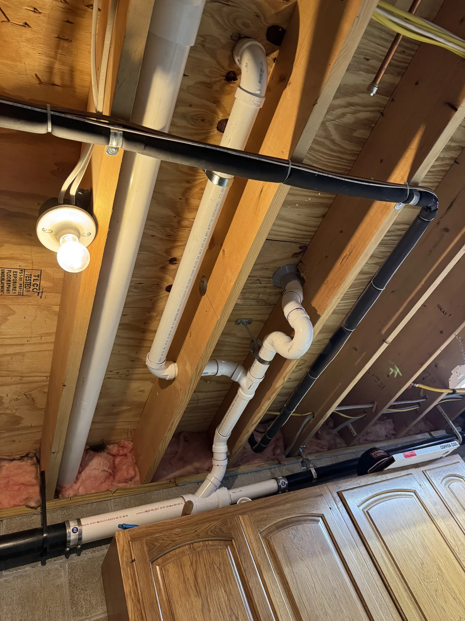 New PVC drain and vent piping run through basement floor joists during a remodel