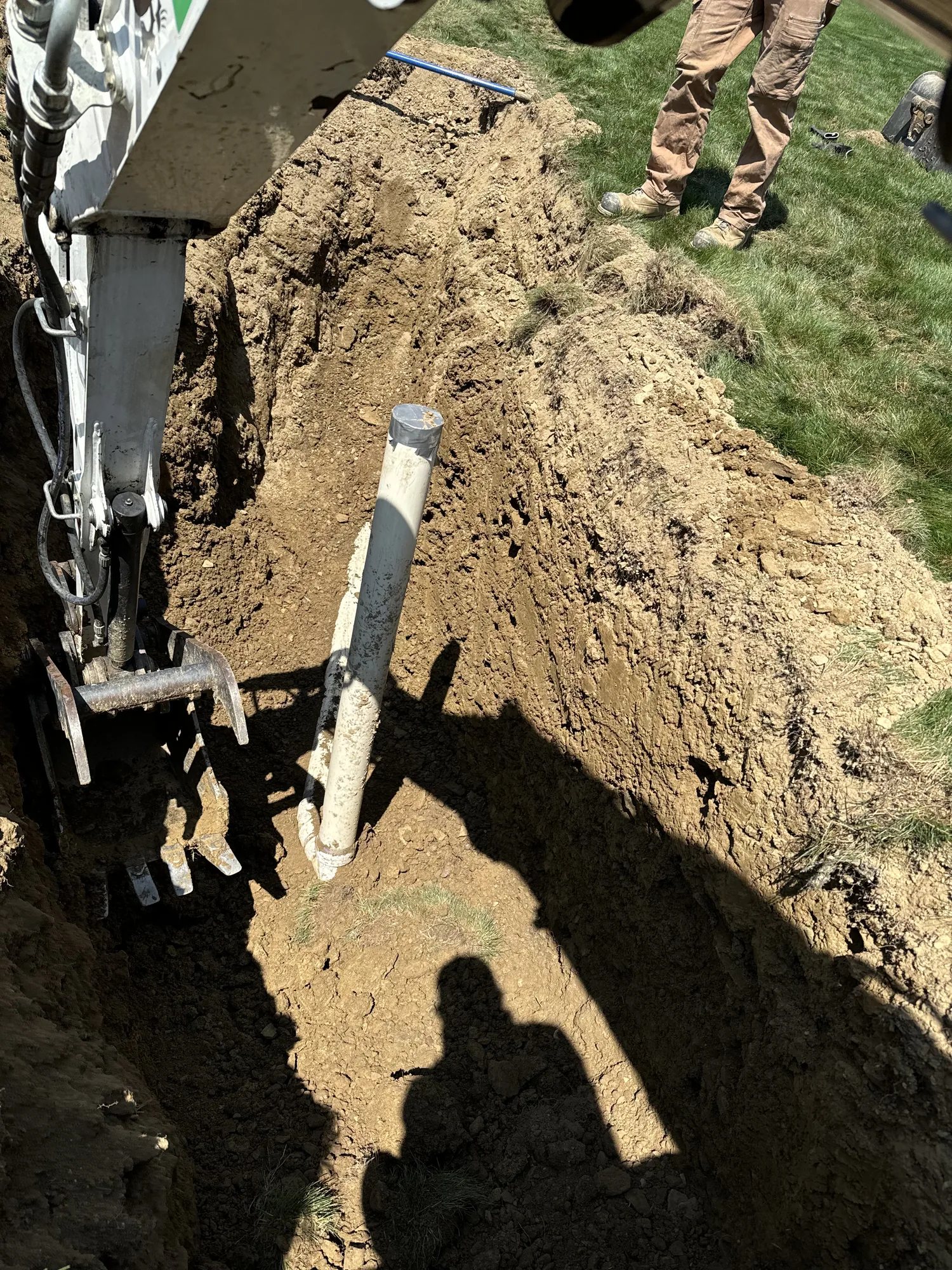 Excavator working an open trench around an exposed PVC utility line at a Pittsburgh area jobsite