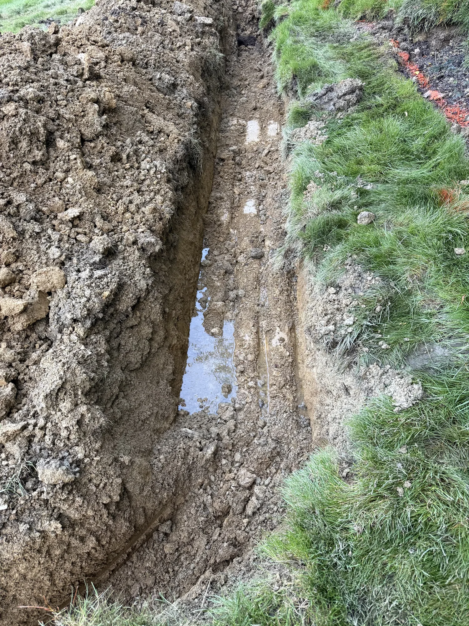 Water collecting in an open trench over a buried line during drainage work on a Pittsburgh lawn