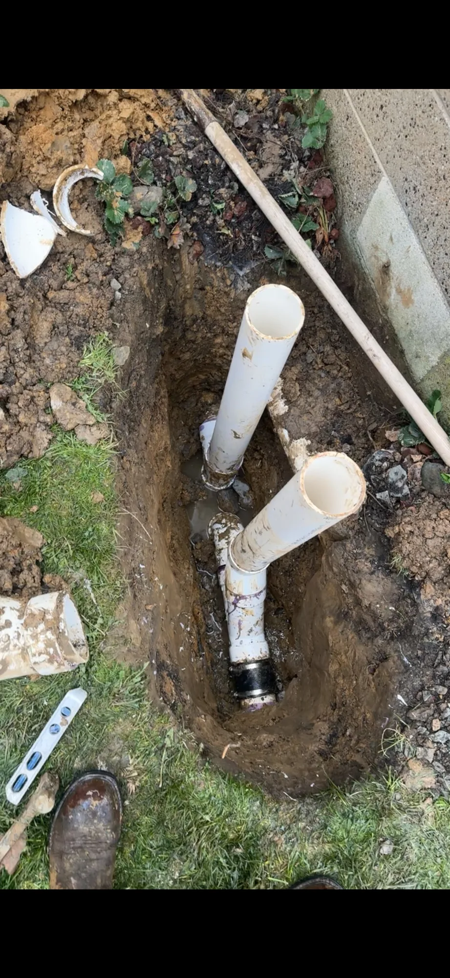 Open pit at a house foundation with new PVC sewer pipe and rubber coupling during a drain line repair near Pittsburgh
