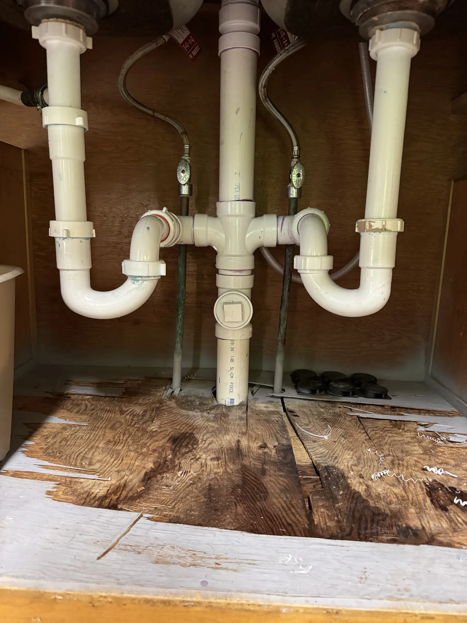 Water damaged sink base cabinet with PVC drain traps and shutoff valves before a kitchen remodel