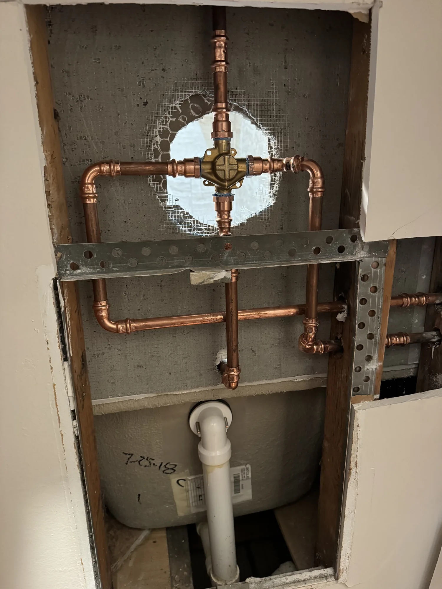 Copper supply lines and brass shower valve roughed into an open wall during a bathroom remodel