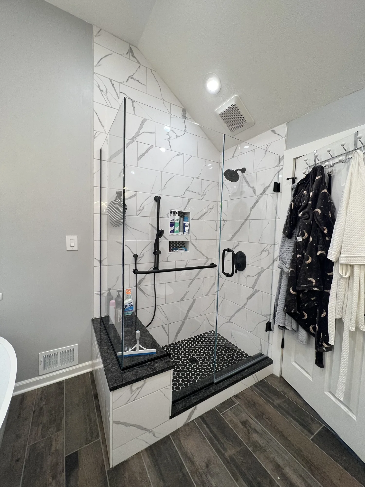 Walk in tile shower with glass panel and black fixtures in a remodeled Allison Park bathroom
