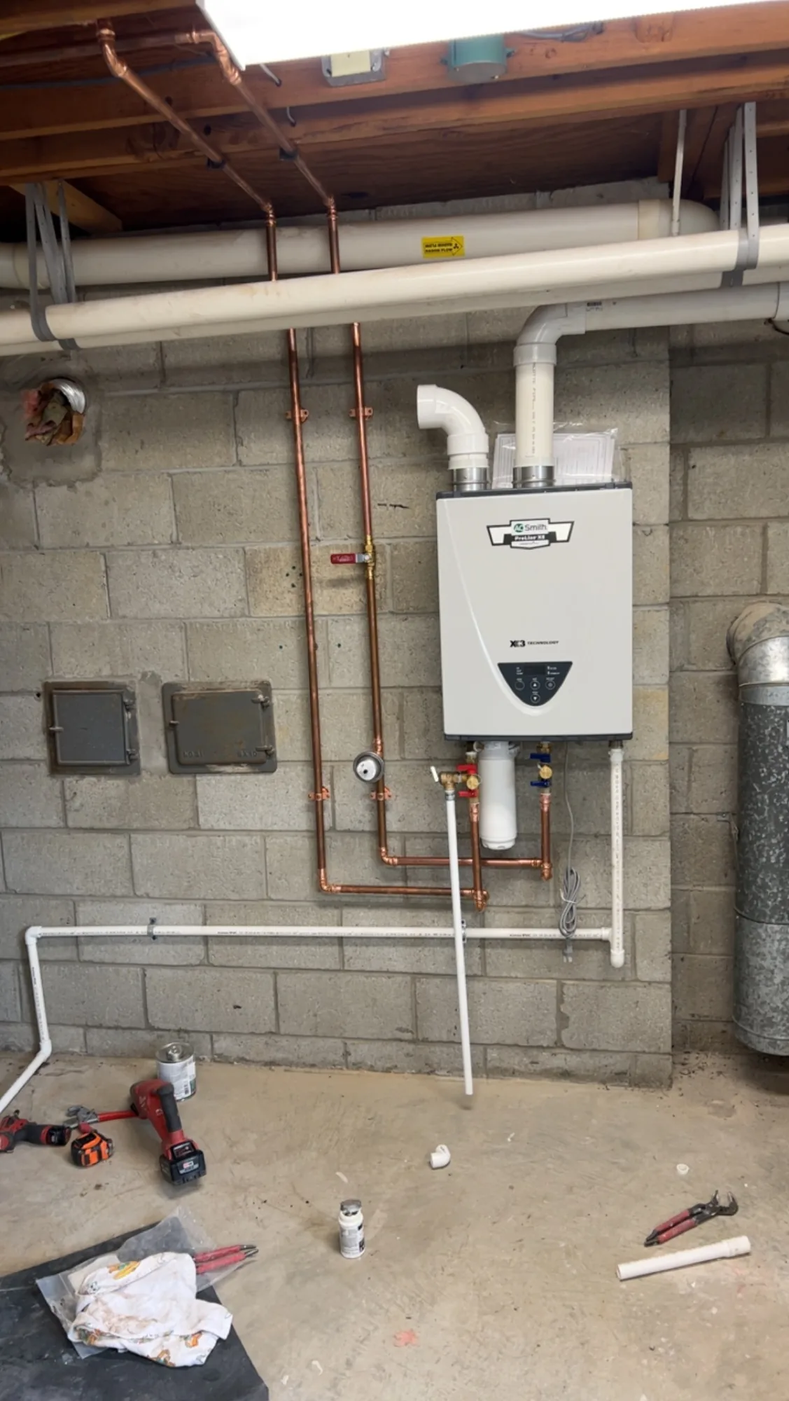 Tankless water heater installed on a basement block wall with new copper water lines and gas supply