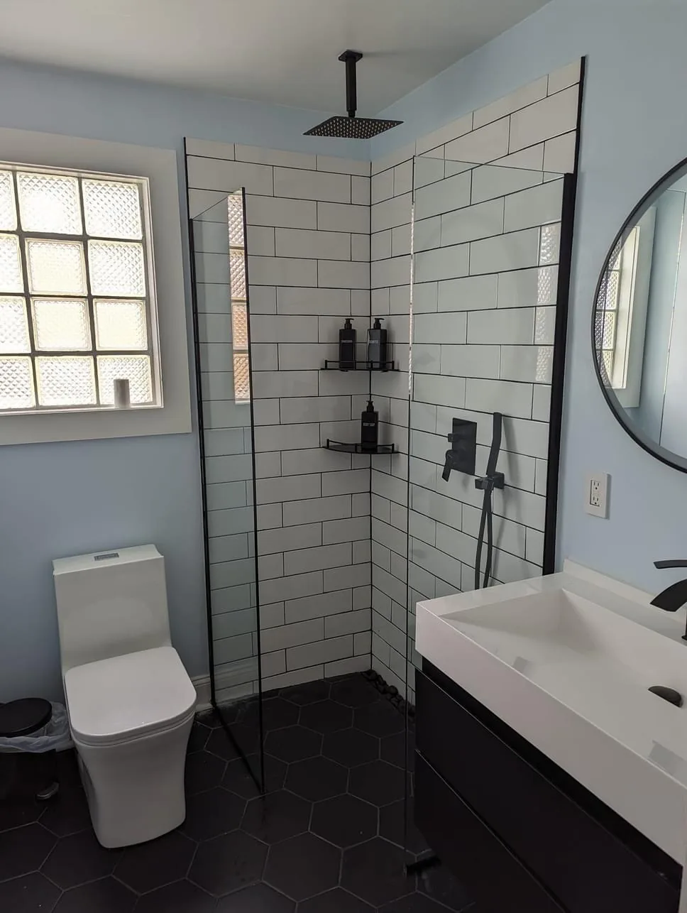 Remodeled bathroom with a white subway tile walk in shower, black hexagon floor tile and a floating vanity